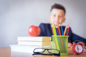 Decorative image representing transitioning from year 6 to 7 of a child sitting in a classroom with an apple resting on some books in the foreground.