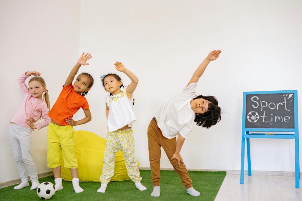 Four young children performing stretching exercises in a classroom. 